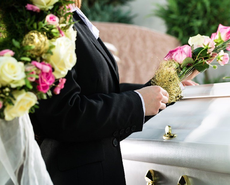 Mourning man and woman on funeral with pink rose standing at casket or coffin